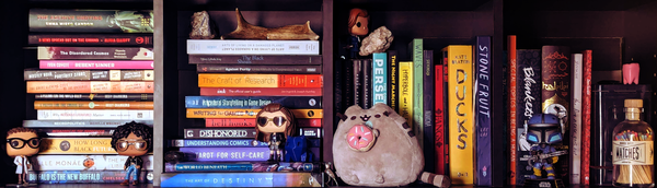 A bookshelf with a variety of genres and knick knacks. 